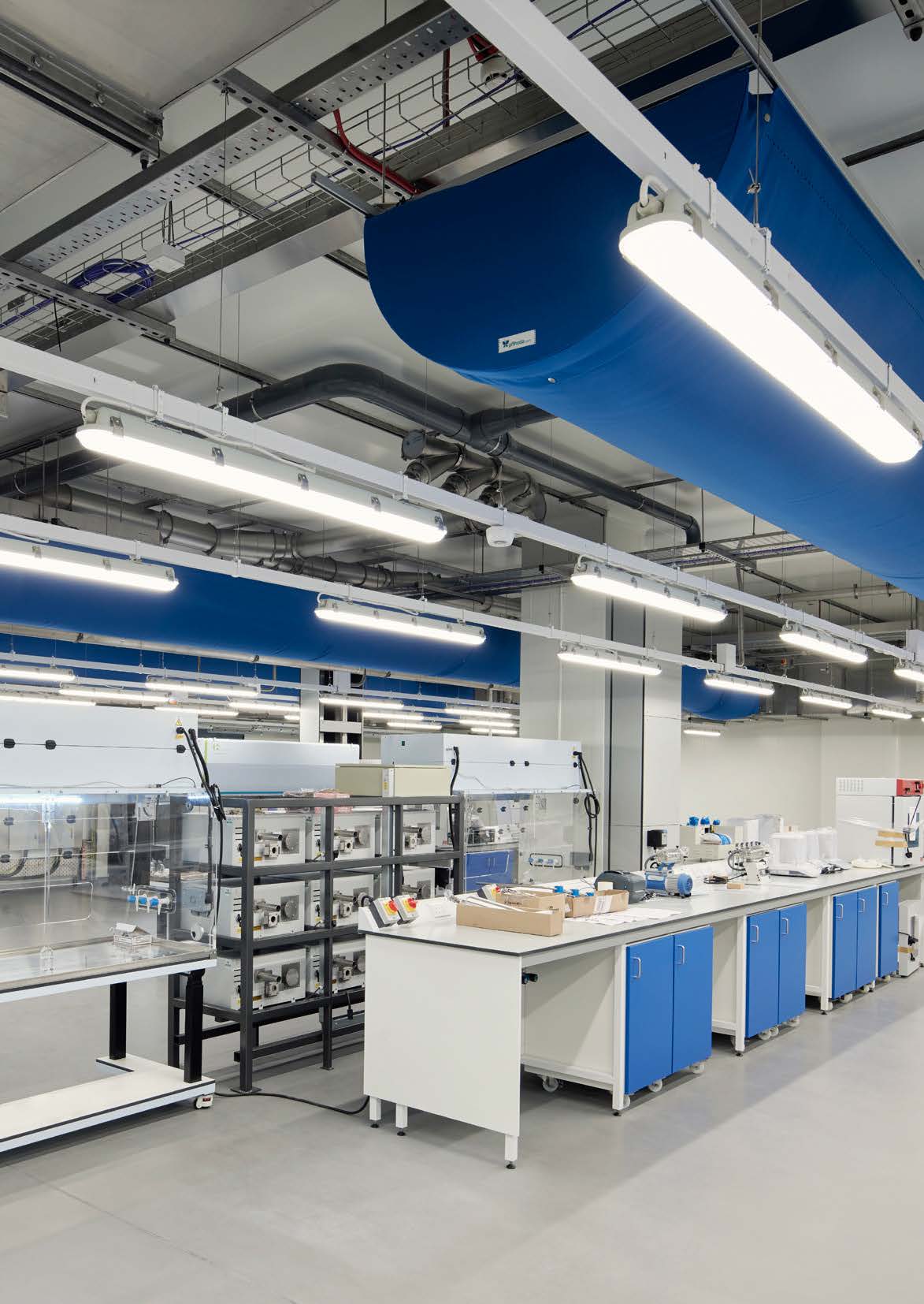 Industrial-style lab with blue ducting, modular workstations, and advanced equipment.